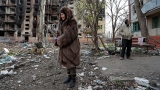 Localnicii stau într-o curte în apropierea unei clădiri rezidențiale distruse din Mariupol, Ucraina